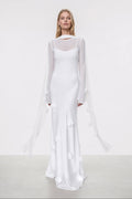 Woman wearing a white dress with sheer sleeves on a plain background