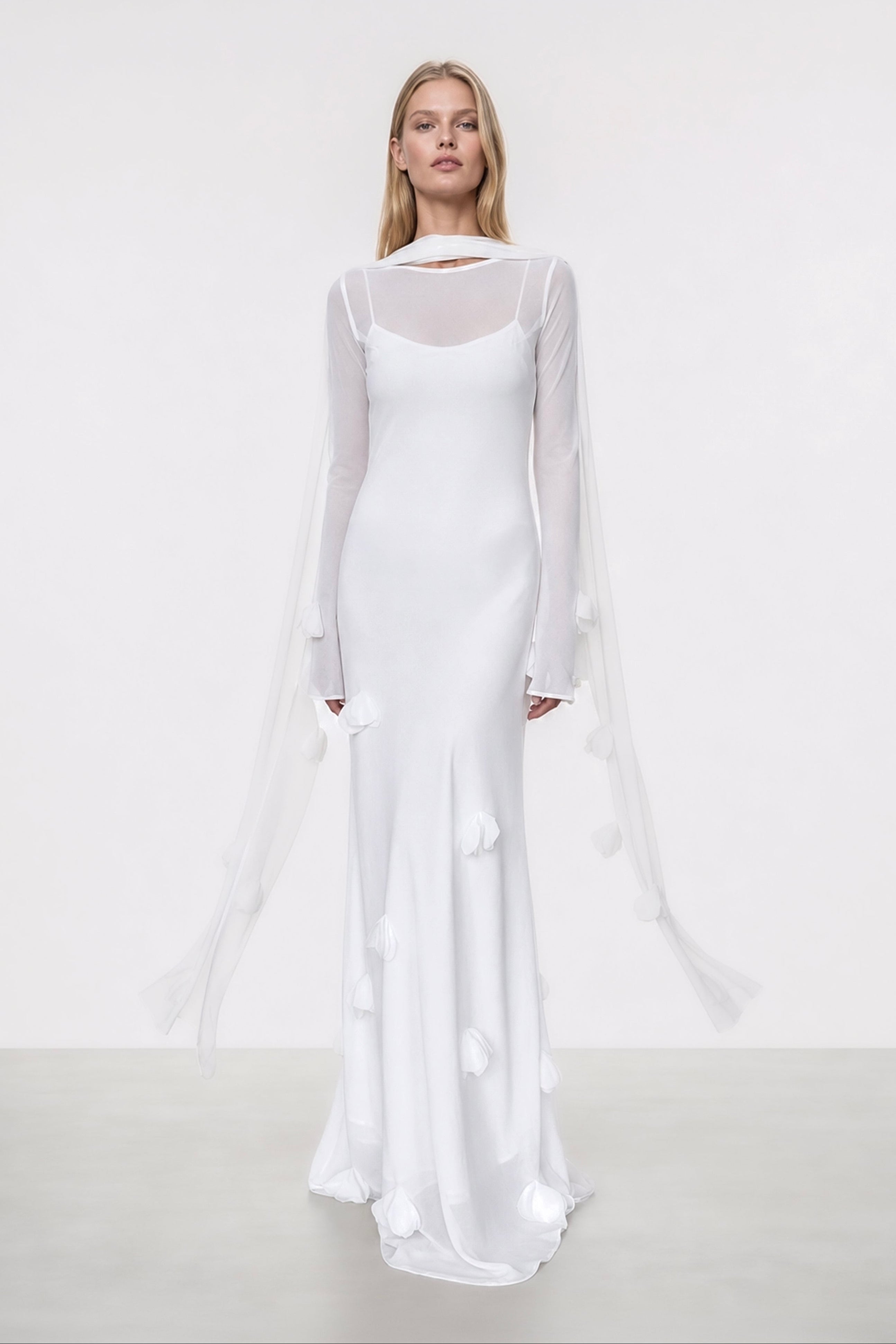 Woman wearing a white dress with sheer sleeves on a plain background