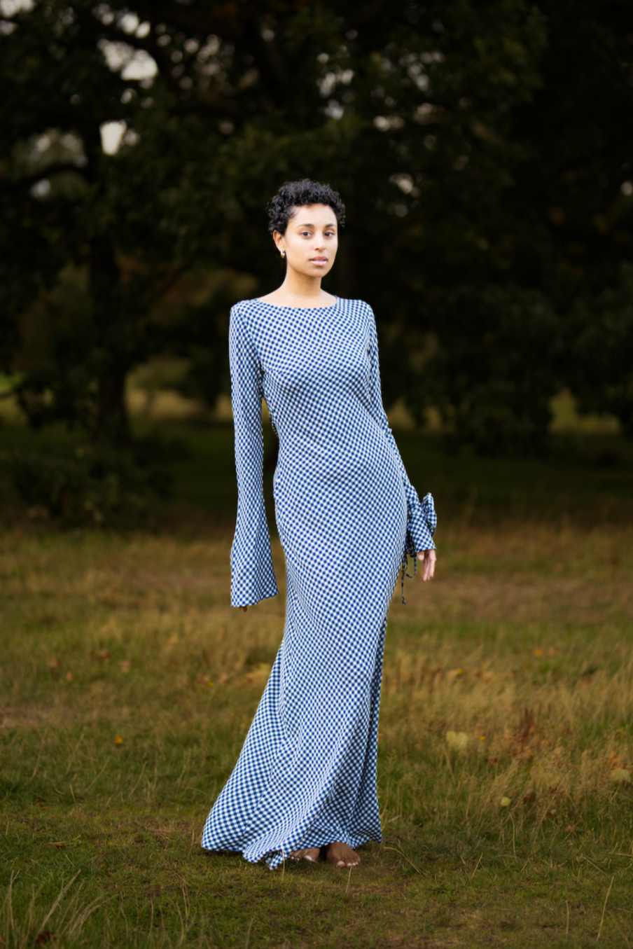Woman in a long blue dress standing in a grassy field with trees in the background